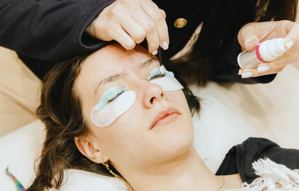 A girl cosmetologist laminates and paints the eyelashes of a teenage client.