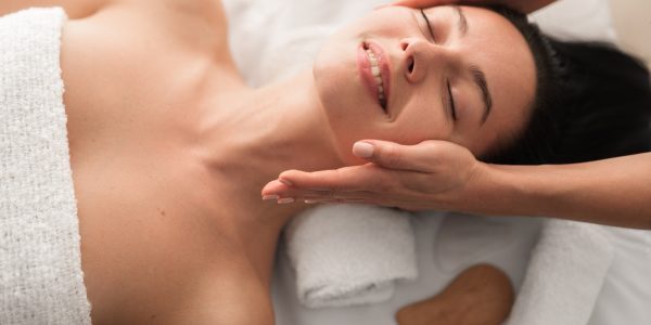 Happy young lady enjoying face massage and smiling during spa session